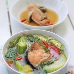 Múc canh chua đầu cá hồi ra tô, rắc rau om ngò gai lên trên mặt và dùng nóng nhé!