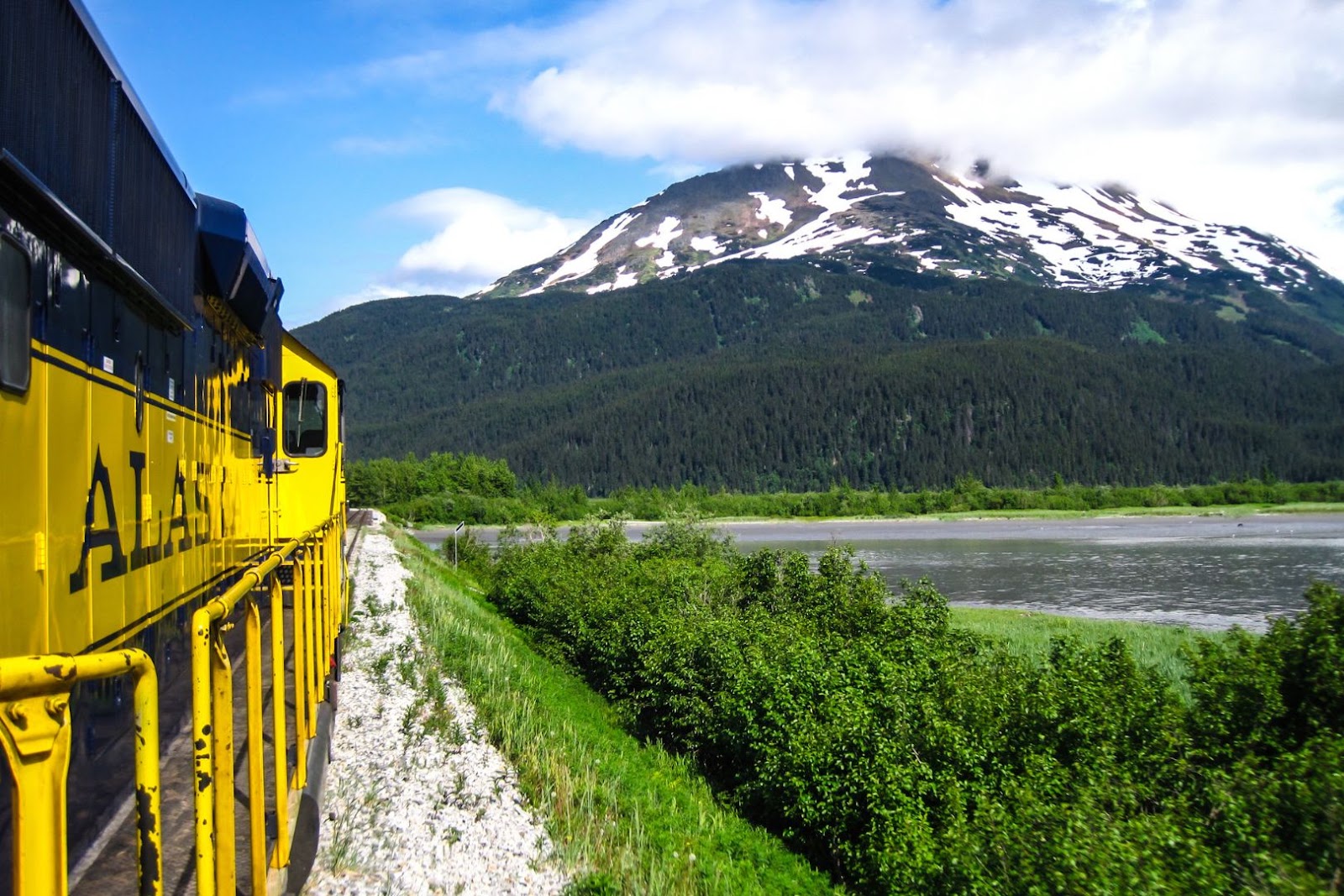 Alaska Railroad train traveling through a scenic mountain landscape surrounded by wilderness.
