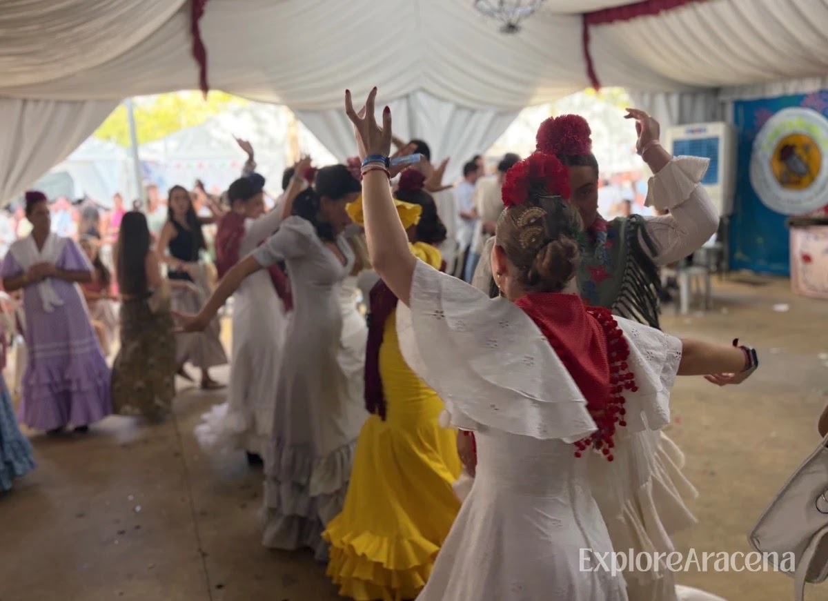 Women in feria dresses dancing sevillanas together inside a crowded caseta.