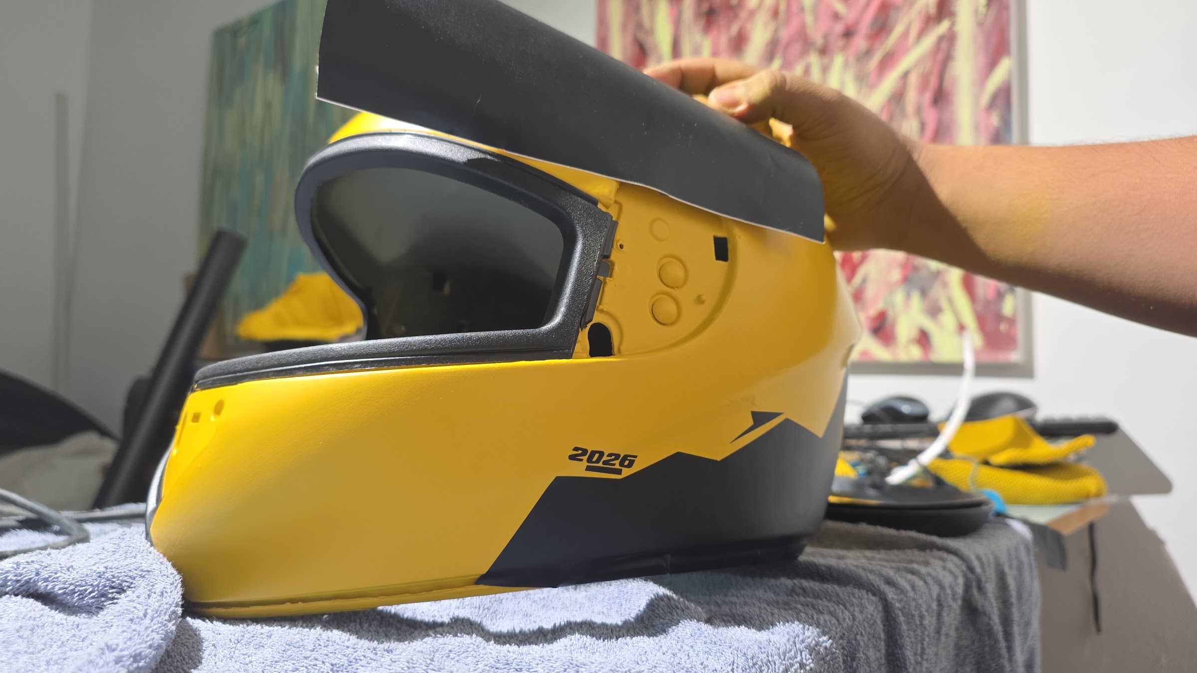 Processo de customização de capacete amarelo, com aplicação manual de adesivo de vinil preto na lateral.