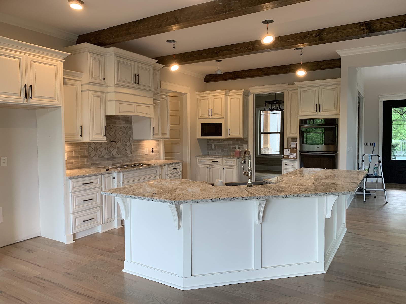 Kitchen with white cabinetry, granite countertops, a large island, and dark wood ceiling beams with pendant lights.