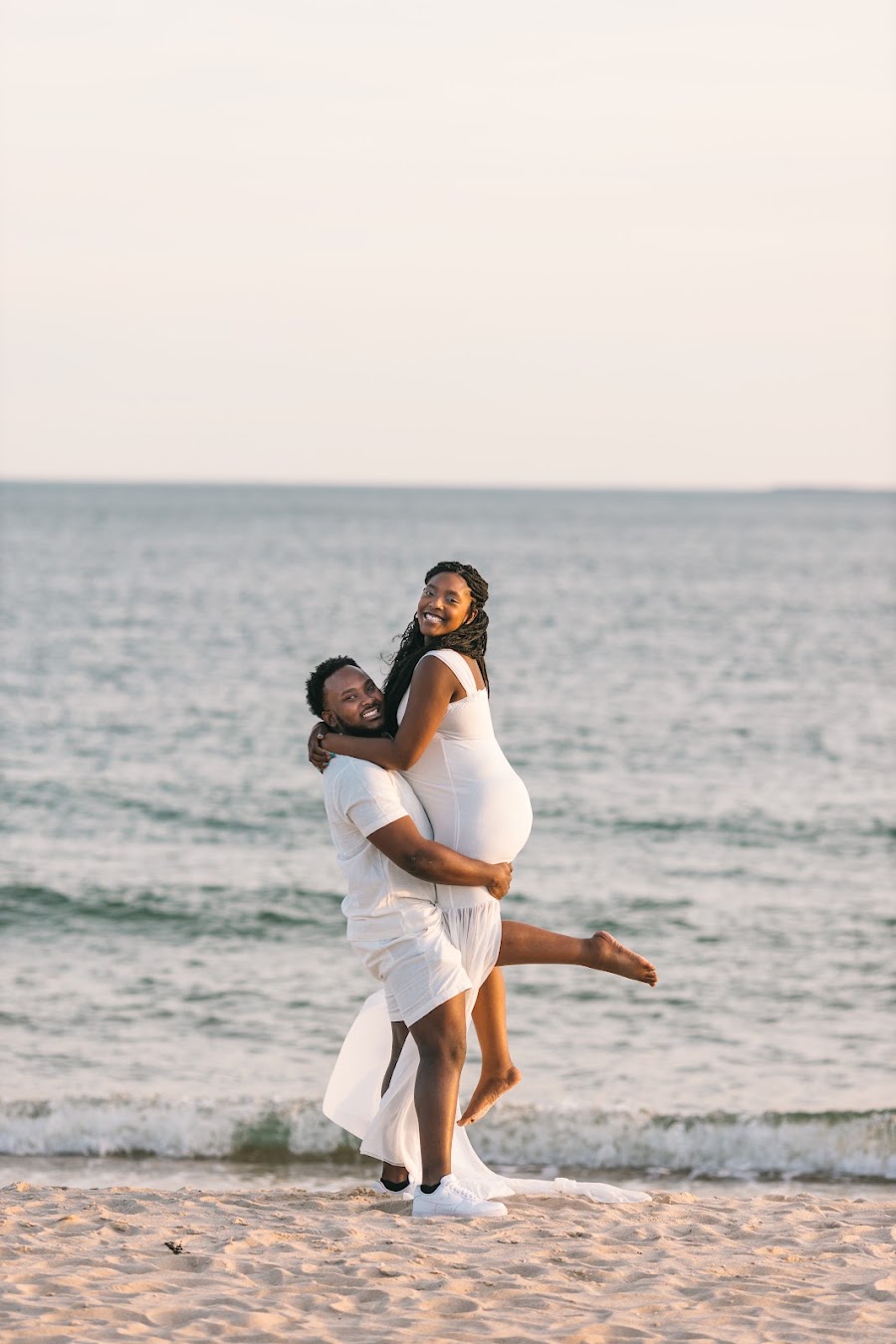 Playful maternity couple lifted on the beach — golden hour