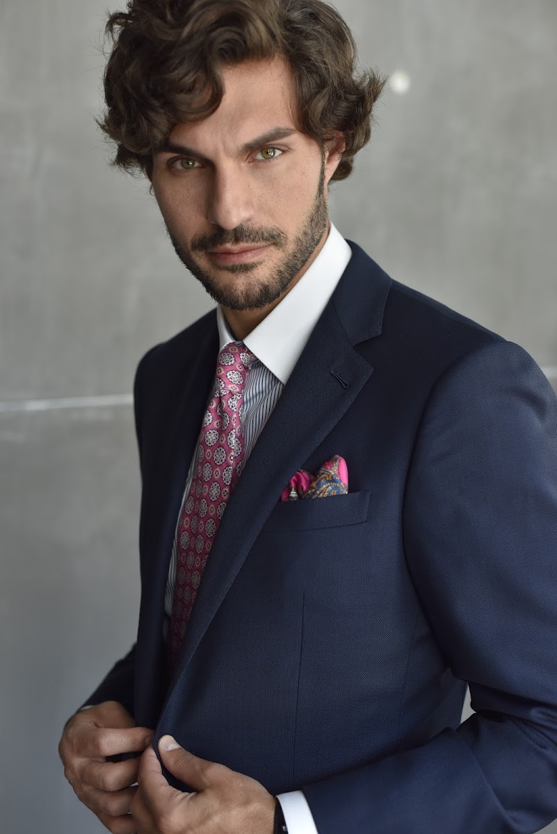 Man in a classic navy suit with notch lapels and a patterned pocket square standing against a concrete wall