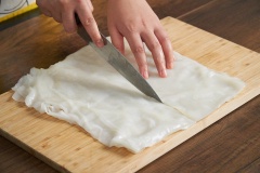 Trải bánh ướt lên thớt cho thật phẳng. Dùng dao cắt đôi bánh ướt để dễ cuốn.