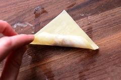 Cho 1 muỗng cà phê hỗn hợp phô mai lên phía dưới cùng của miếng hoành thánh. Dùng tay phết hỗn hợp trứng lên các rìa của vỏ bánh. Đặt lên tay rồi cuộn lại như hình.