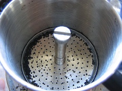 Khi nước sôi, cho 1 muỗng canh nước vào phin để làm ẩm cà phê và làm cà phê nở ra.