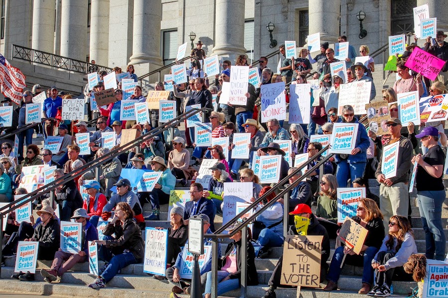 A large crowd seated and standing on the Capitol steps holding “Utahns Against Power Grabs” and other signs