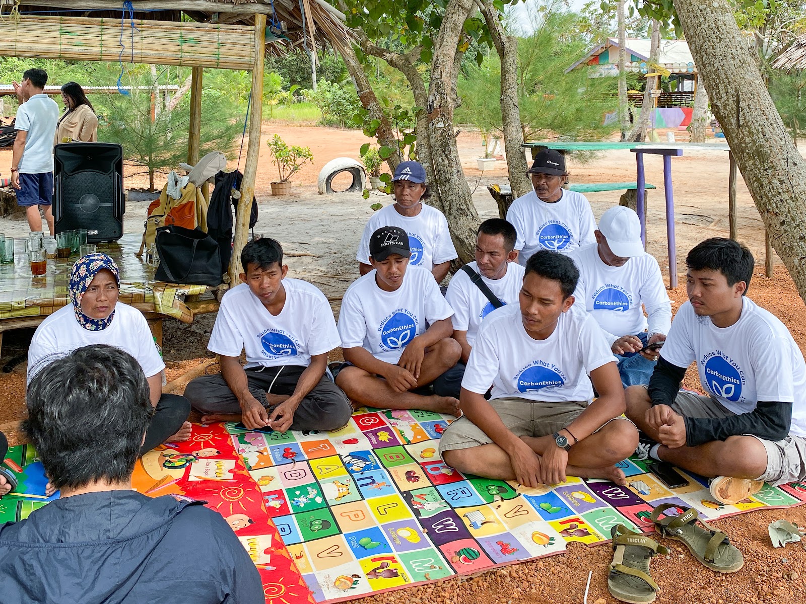PPDL Farmers sitting on colorful rug on the beach paying attention to CarbonEthics' teams' instructions