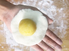 Tiến hành chia bột thành các phần bằng nhau, mỗi phần có khối lượng 50gr. Cũng dùng màng bọc thực phẩm đậy lại phần bột chưa làm để bột không bị khô. Sau đó lấy một miếng bột cho ra mặt phẳng, dùng lòng bàn tay ép dẹt miếng bột, nặn thành hình tròn, rìa ngoài mỏng hơn ở giữa. Sau đó lấy một phần nhân đã làm ở trên đặt vào giữa miếng bột, gói lại.