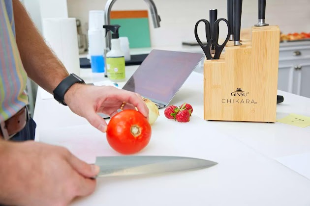 Manos sosteniendo un tomate y un cuchillo del juego de cuchillos de bloque de bambú de 8 piezas Ginsu Chikara