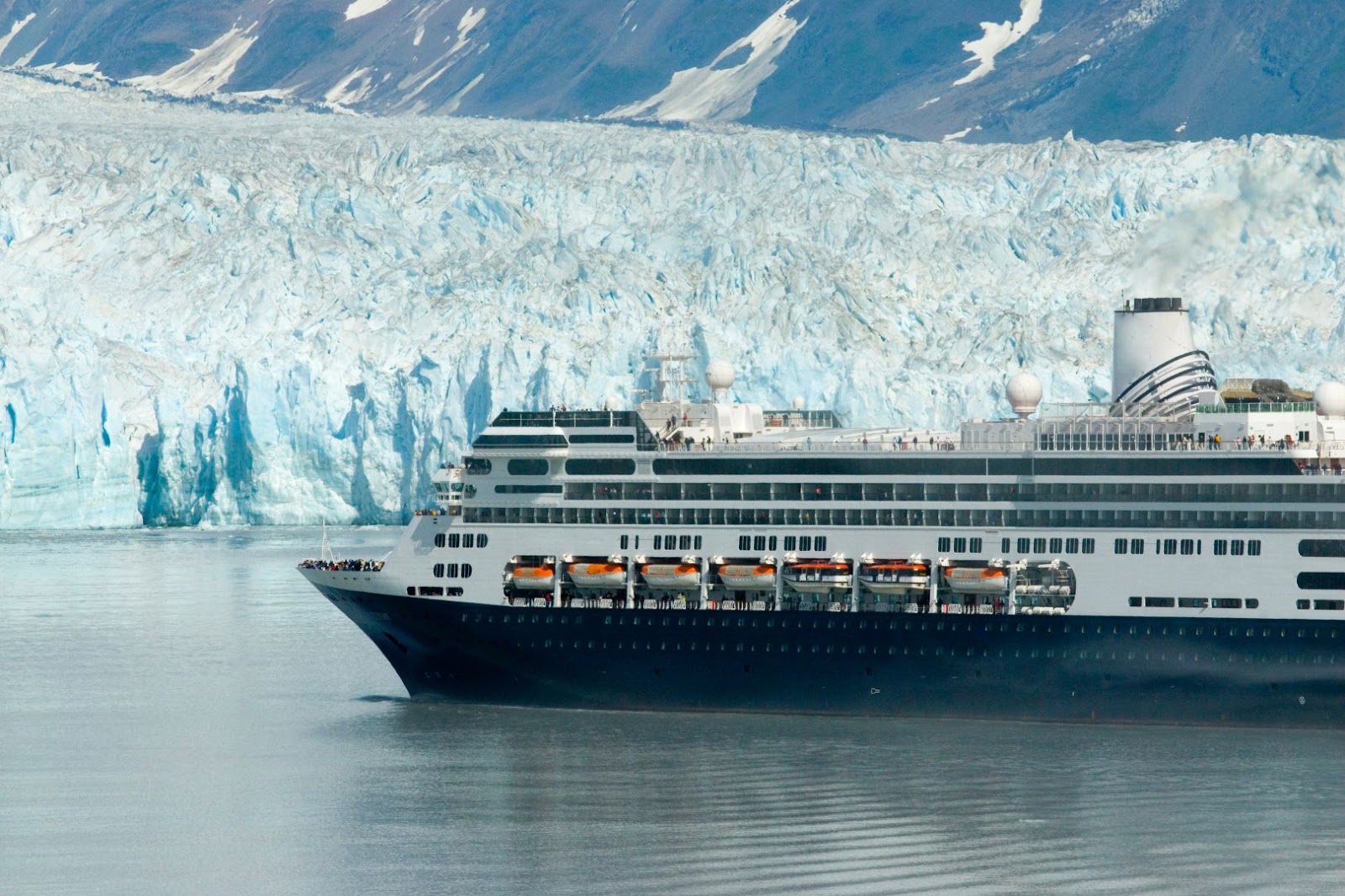 Cruise ship sailing near a massive Alaska glacier with snow-covered mountains in the background.