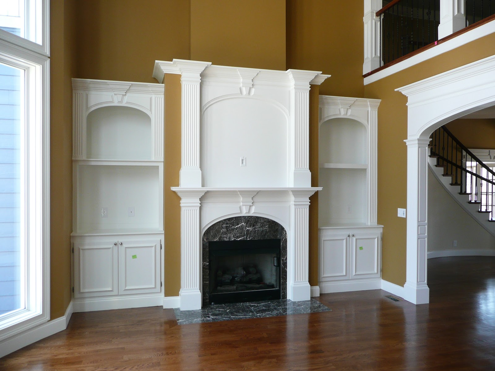 Interior living area with a white fireplace mantel, dark marble surround, and built-in white shelving on either side. Mustard-colored walls and wood floors.