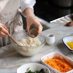 Cho 3 chén cơm dẻo vào thố lớn, thêm vào 1/2 muỗng canh mè trắng rang, 1/2 muỗng cà phê muối và 1 muỗng canh dầu mè vào trộn đều.