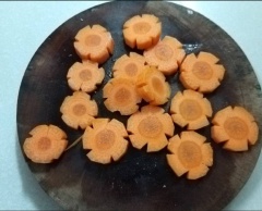 Gọt vỏ cà rốt, rửa sach, để ráo. Dùng dao bổ dọc củ cà rốt 1 đường, cắt xéo thêm 1 đường song song với đường vừa cắt, lấy sợi cà rốt ra tạo rãnh. Tỉa 5 đường trên thân cà rốt. Sau đó, đặt củ cà rốt xuống thớt, cắt khoanh dày 5mm. Sau khi cắt ta được hoa cà rốt như hình.