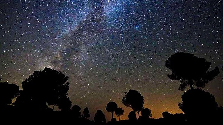 The Milky Way stretching above the silhouetted trees of the Sierra de Aracena beneath a clear night sky.