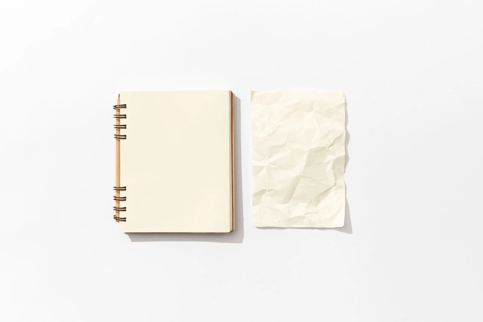 Flat lay of an open spiral notebook and a crumpled paper on a white background, perfect for mockup designs.