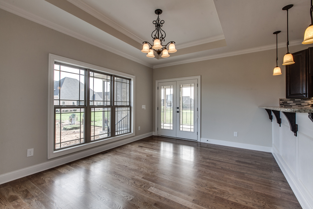 An empty dining area with hardwood floors, a tray ceiling with a chandelier, a large window, and white French doors.