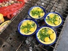 Nhóm lửa bếp than, sử dụng chén làm bánh bèo, đập mỗi chén 4 quả trứng cút, thêm hành lá cắt nhỏ lên trên mặt.