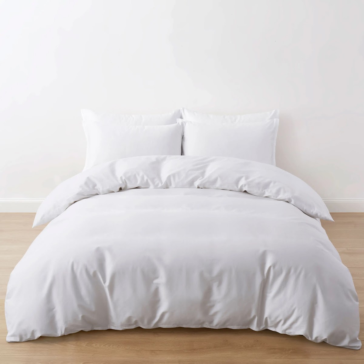 White duvet cover and pillows on a wooden bed against a plain wall, front view