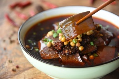 Bày trí huyết heo chua nóng: Cho huyết heo ra tô, dội chén sốt vừa pha lên trên, rưới thêm ít nước dùng đã đun, nêm nếm cho vừa miệng. Thêm ít sốt ớt đậu cay, đậu nành chiên và hành lá, dùng nóng.