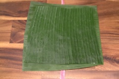 Cách gói bánh tét chuối: Đặt 1 sợi dây nylon lên mặt phẳng, trải lá chuối ra, mặt xanh đậm hướng xuống dưới, đặt tiếp một miếng lá chuối lên, mặt xanh đậm hướng lên trên (thoa ít dầu ăn lên mặt lá để chống dính). Múc 2/3 chén gạo nếp đậu đen đã sên cho vào giữa, dàn mỏng đều (10x12cm).