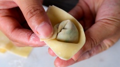Tiếp theo phết thêm 1 lớp nước mỏng lên mép trái bên trong của miếng hoành thánh rồi cuốn và gấp mép phải lên phía trên, miết nhẹ để hoành thánh kết dính. Làm lần lượt như vậy cho đến hết nhân và lá hoành thánh.