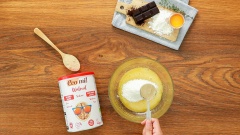 Cho lần lượt 2 cái lòng đỏ trứng gà, 30gr đường xay, vào tô dùng phới lồng trộn đều rồi rây 15gr bột bắp vào tô cùng 15gr bột óc chó Ecomil.