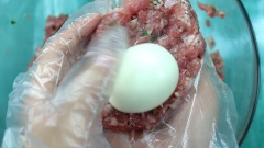 Cho thịt băm vào tô cùng với 1 muỗng cà phê muối, 2 muỗng cà phê tiêu, 2 muỗng cà phê đường, 2 muỗng cà phê hạt nêm và 1 muỗng canh hành lá cắt nhỏ. Trộn đều hỗn hợp. Lấy một nắm thịt vừa đủ, ấn dẹt rồi cho trứng vào giữa, bọc thịt đều quả trứng.