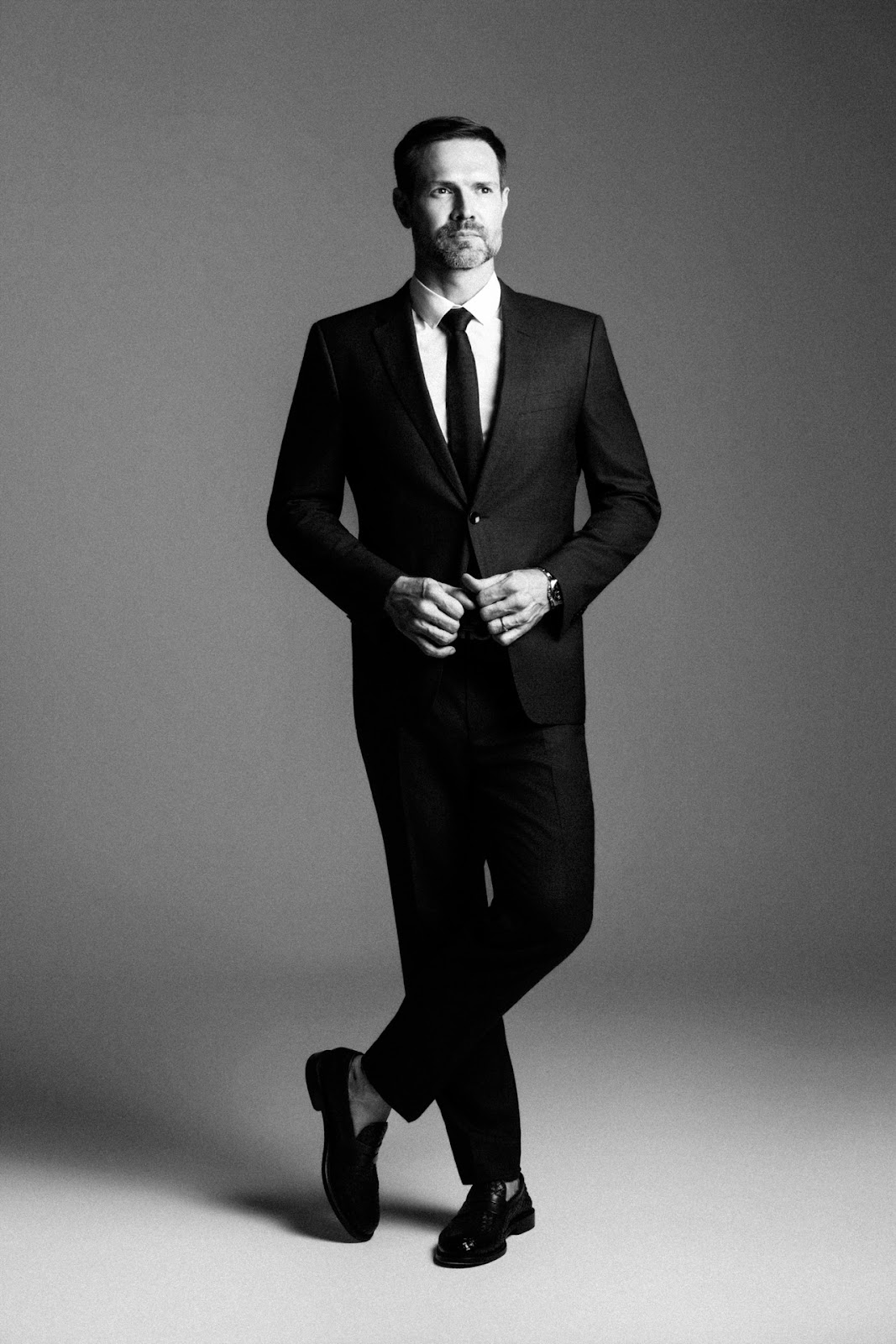 Retrato masculino de corpo inteiro em preto e branco com terno e postura cruzada.