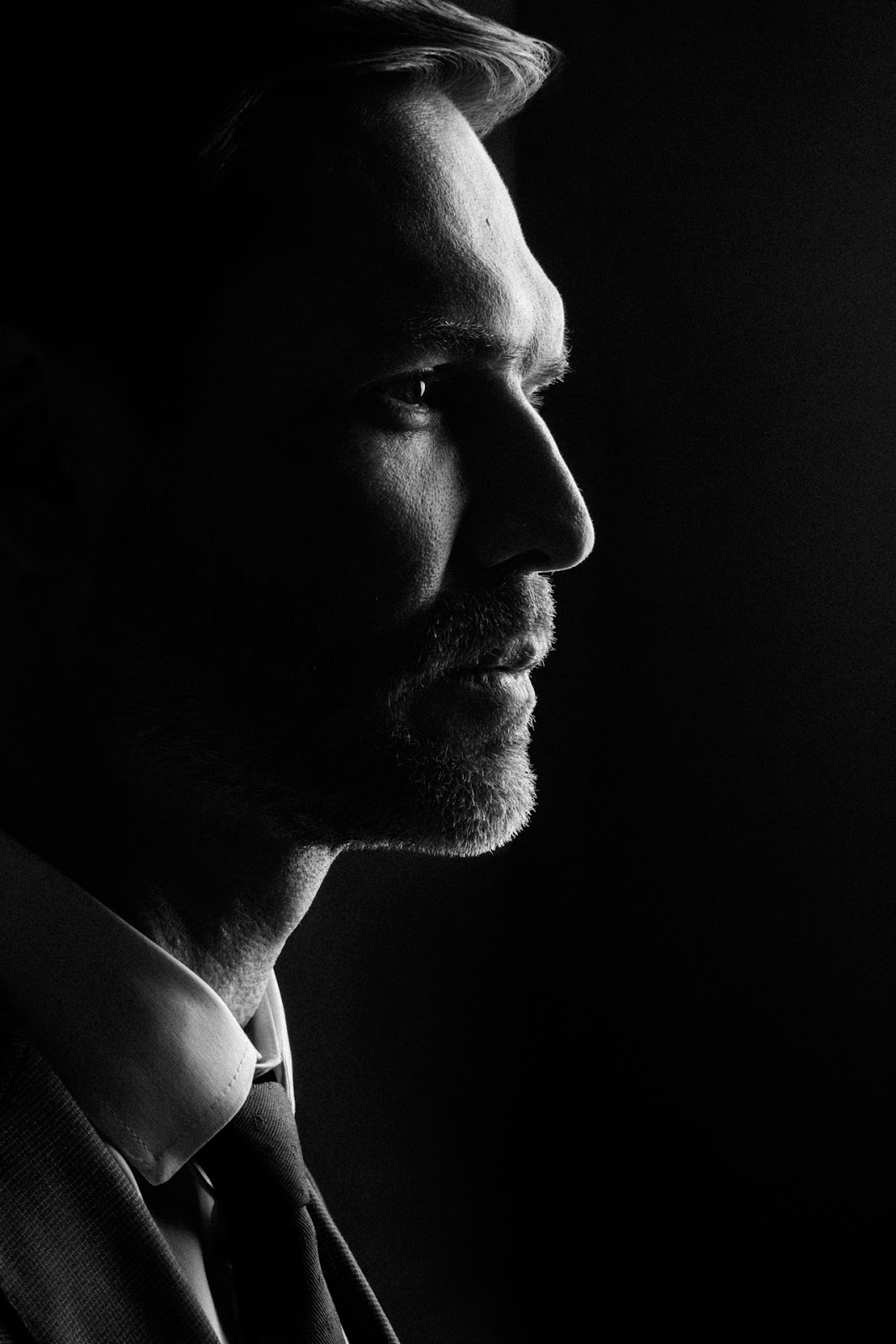 Perfil masculino em preto e branco com luz de recorte e fundo escuro.