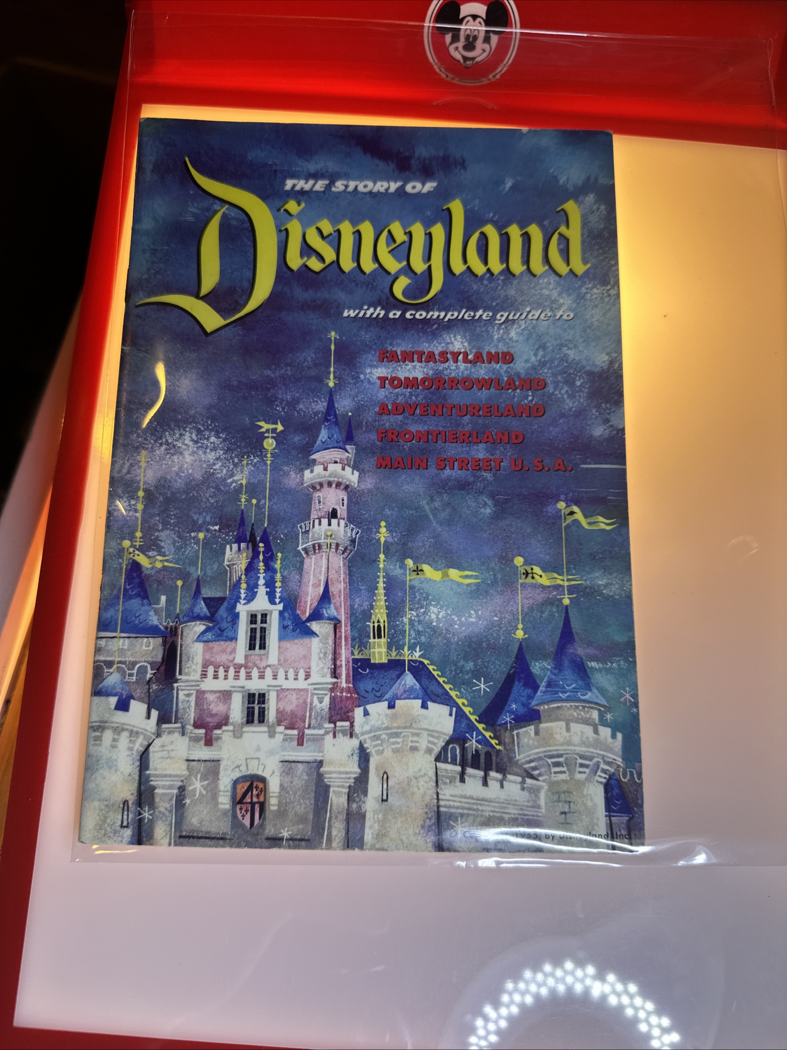 1955 Disneyland opening-year souvenir guidebook with stylized blue and purple Sleeping Beauty Castle cover, protected in plastic sleeve