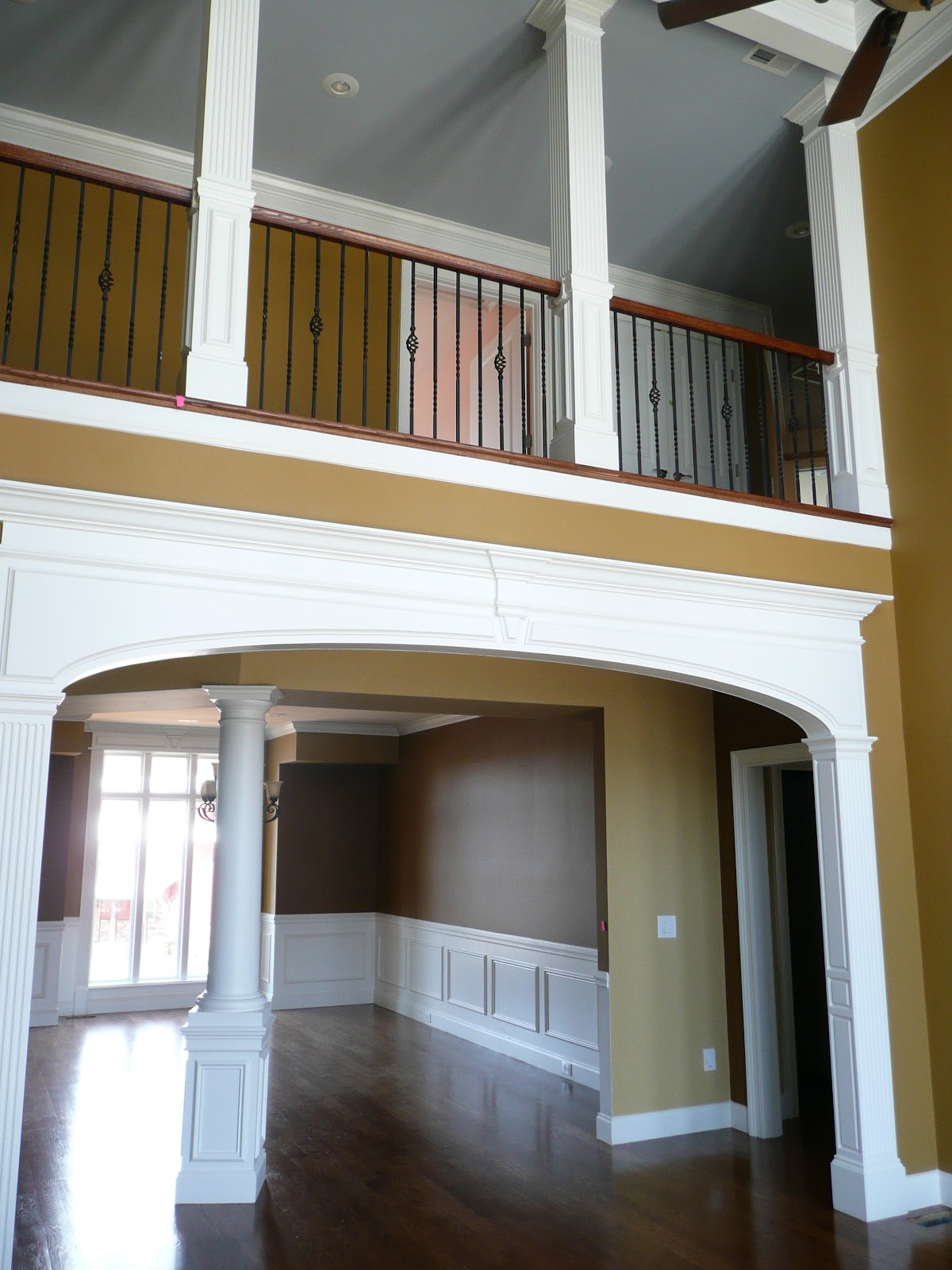 Interior view of a home featuring a large white decorative archway and a second-story balcony with a dark metal railing and wooden handrail.