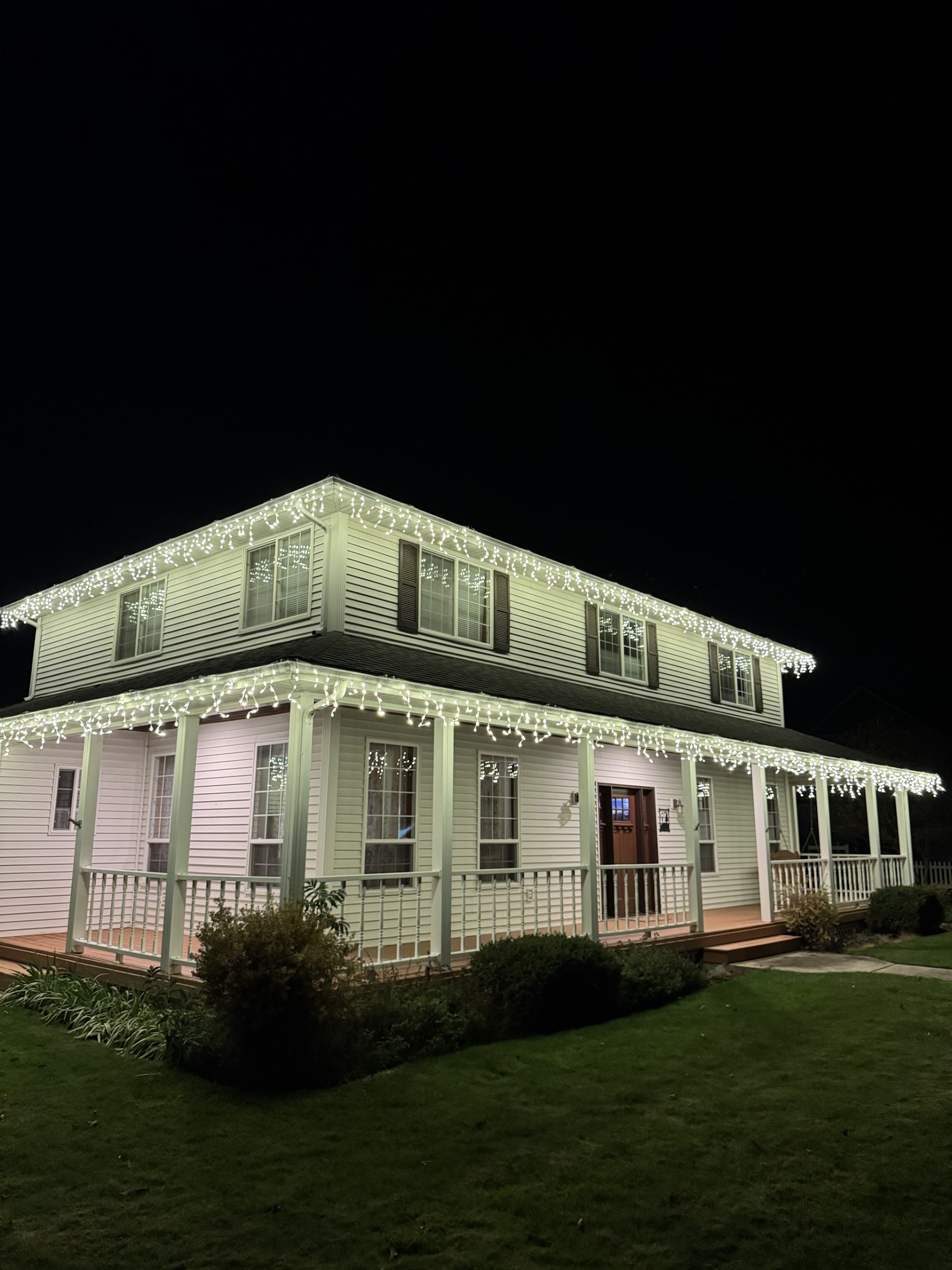 Real completed icicle lighting wrapping the rooflines of a white home