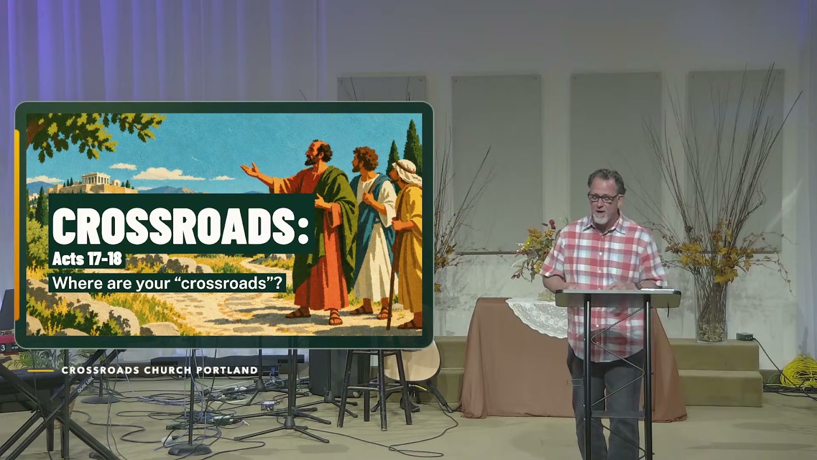 Sean Thome teaching during the October 18 Crossroads service beside the Crossroads: Acts 17–18 message graphic.