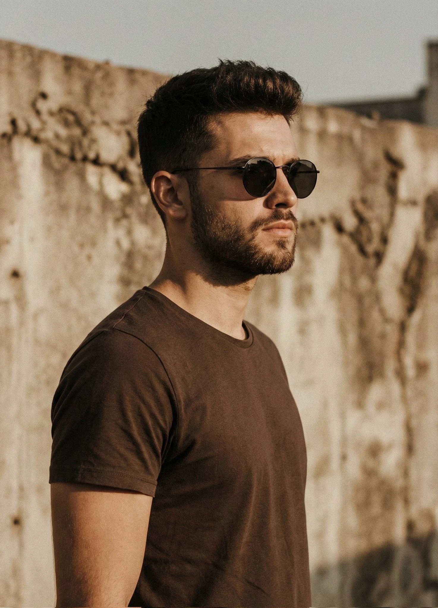 Un retrato cinematográfico de un hombre apuesto con el pelo corto y bien peinado, barba recortada y vestido con una sencilla camisa marrón...