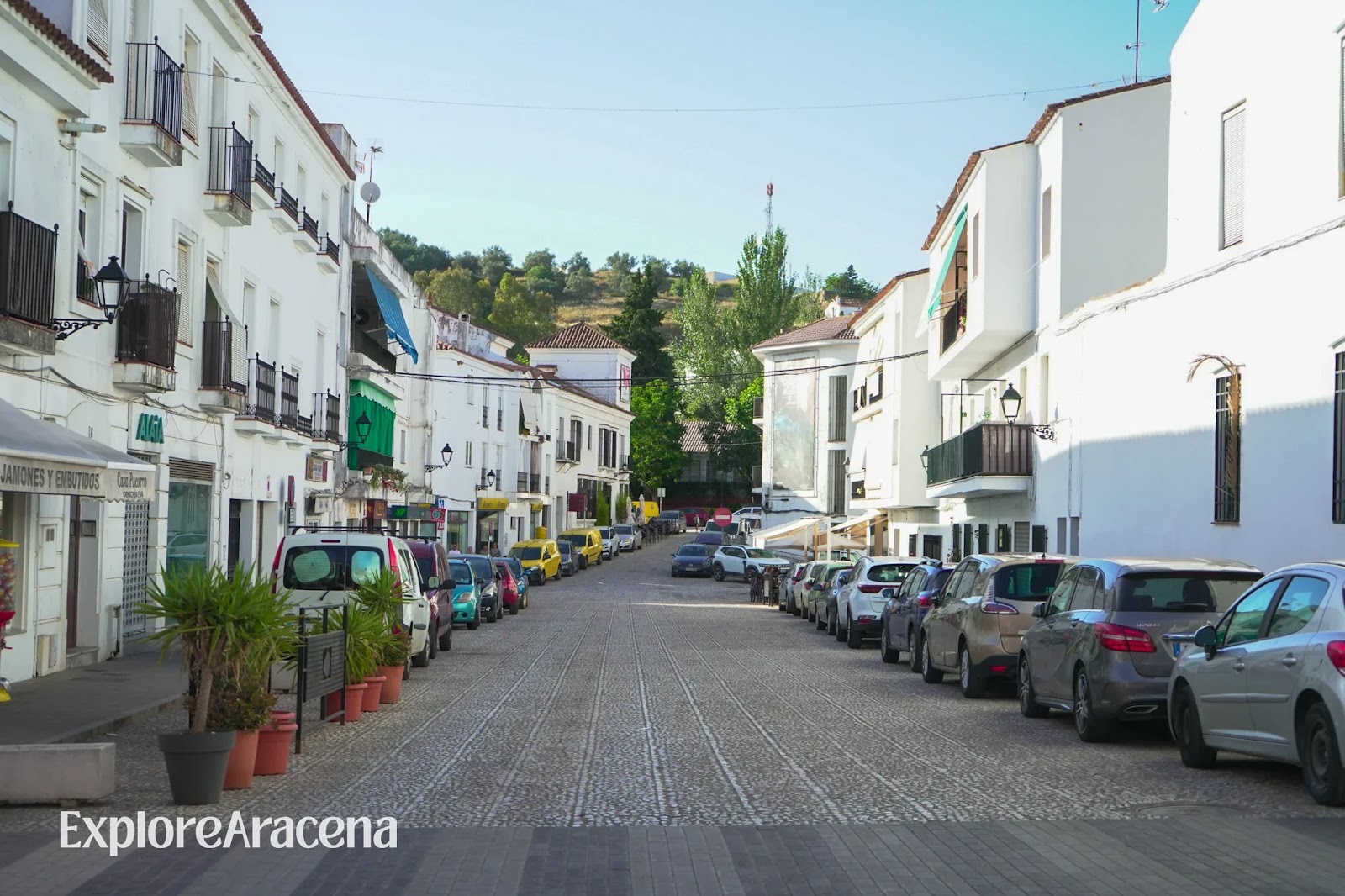 Parked cars lining a street between whitewashed buildings in Aracena.