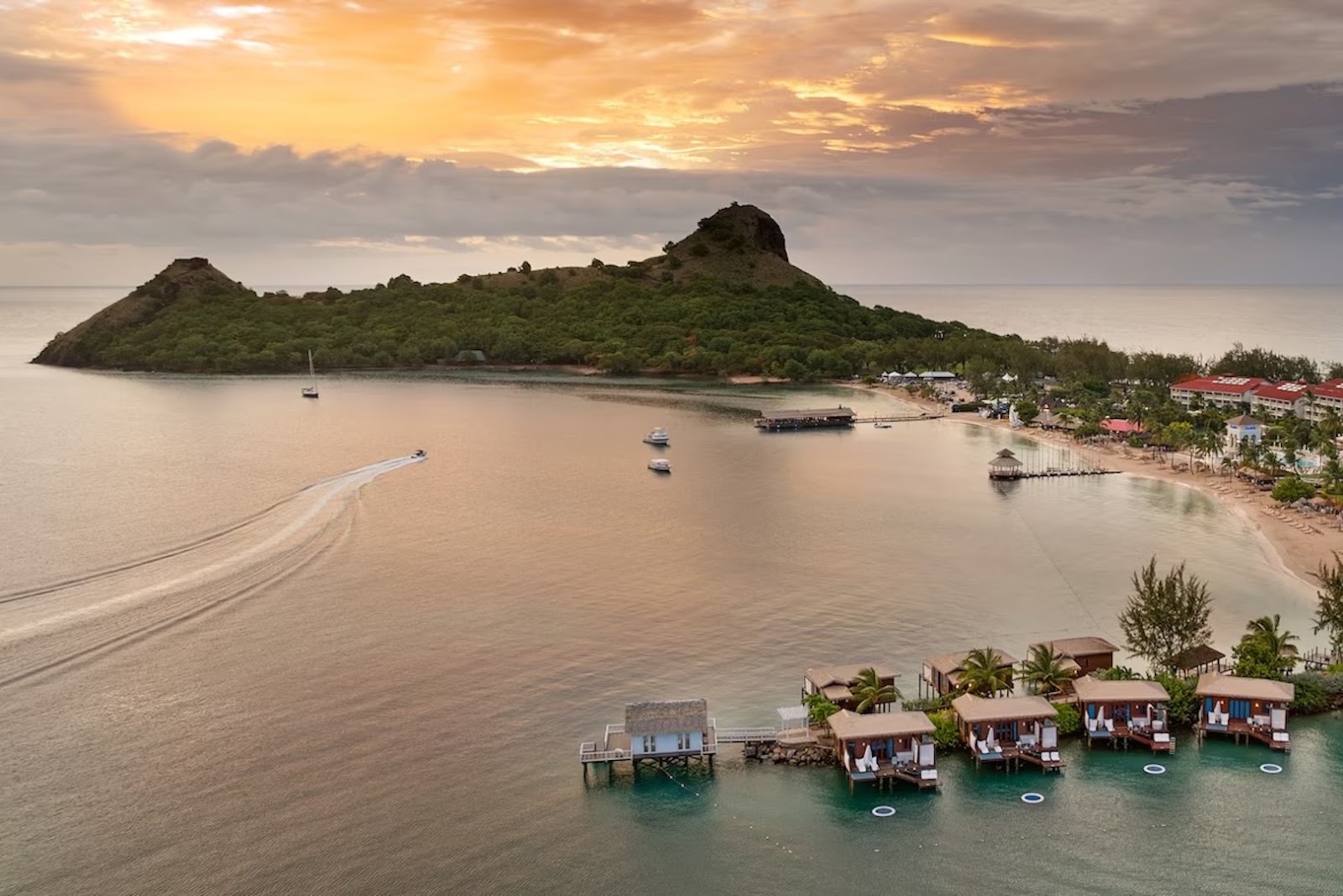 Overwater bungalows at Sandals Grande St. Lucian extending into the Caribbean Sea with mountainous St. Lucia scenery in the distance.