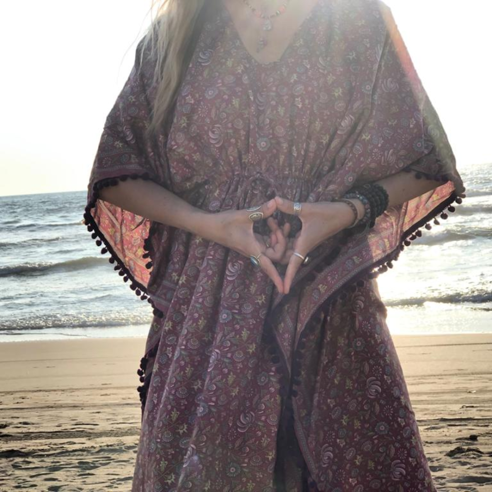 Femme en tunique bordeaux sur la plage, geste du cœur avec les mains