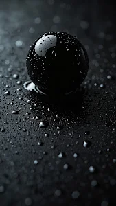 Glossy black sphere covered in water droplets on dark surface