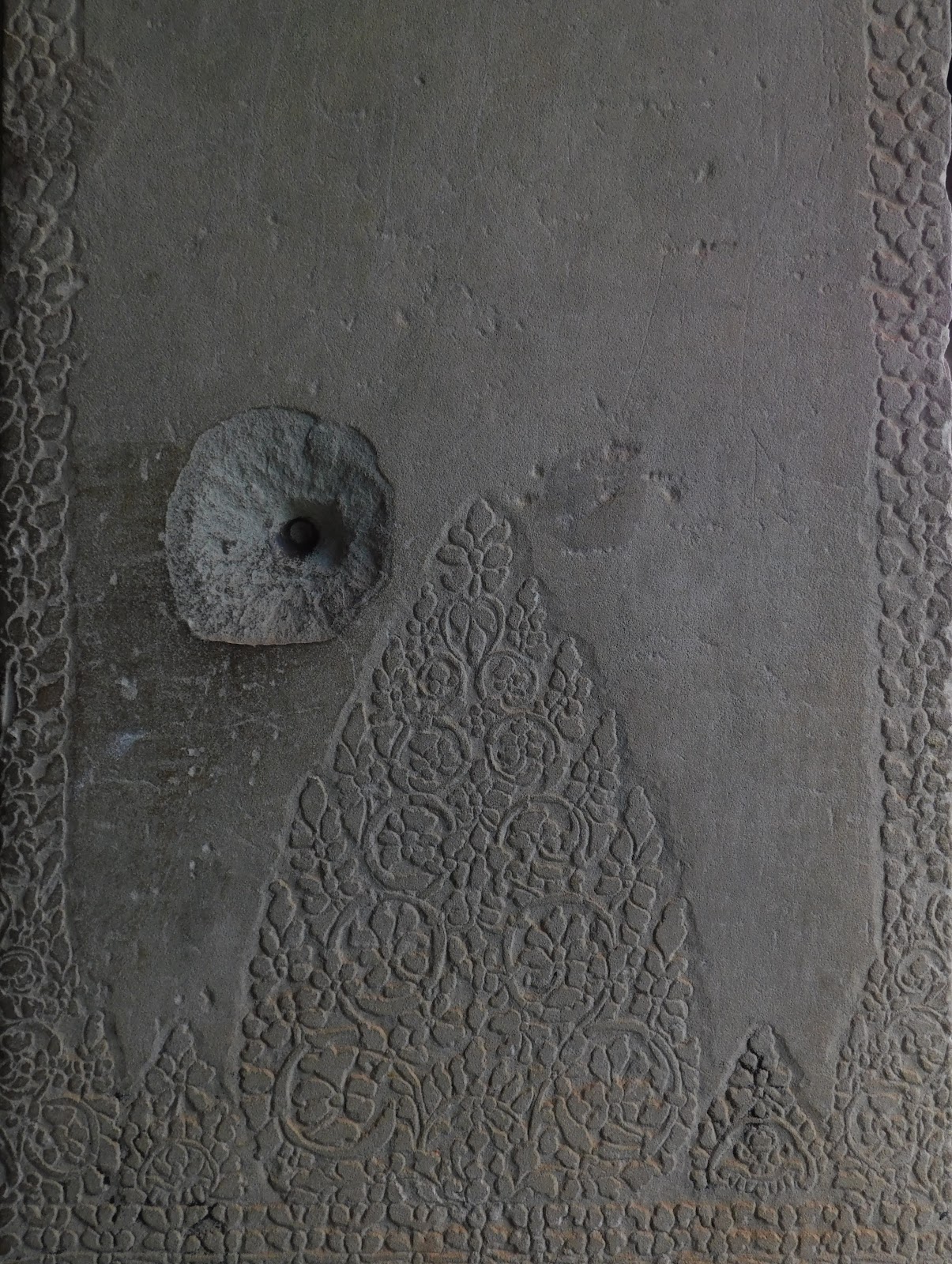 A wall with some bas relief carvings with crater-like damage
                 from a bullet in the center of the photo