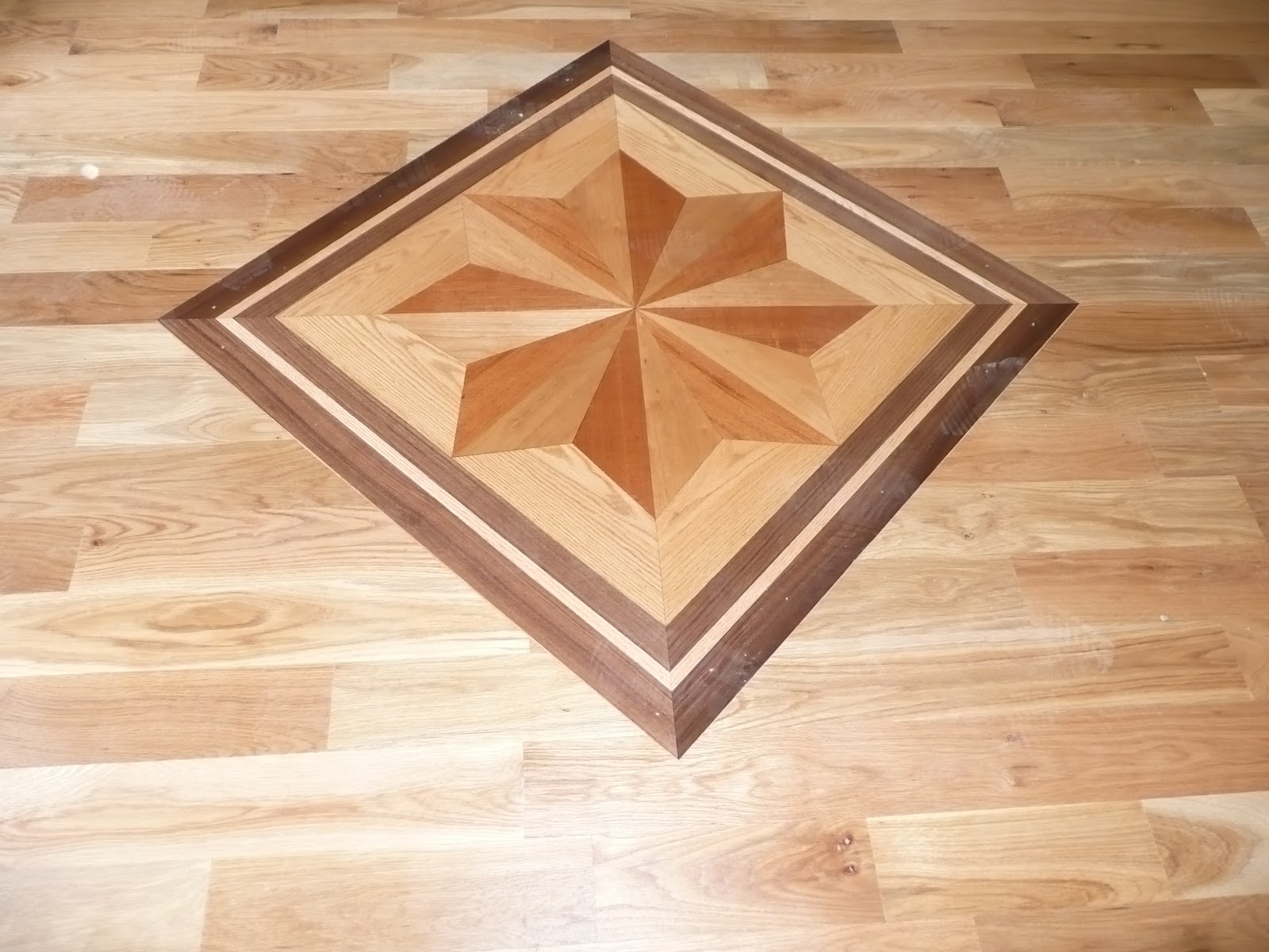 A decorative wood floor inlay featuring a star pattern in multiple shades of wood.