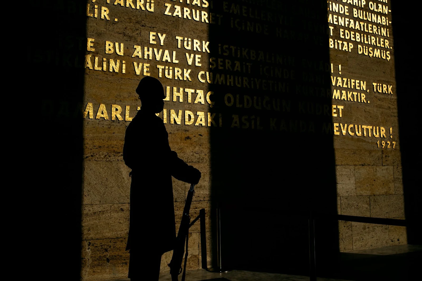 Silhouette of a soldier holding a rifle, displayed against a wall with historical inscriptions in Ankara, Türkiye.