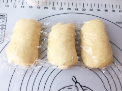 Sau khi ủ, chia khối bột thành 3 phần đều nhau, bọc màng thực phẩm, ủ tiếp 15 phút.