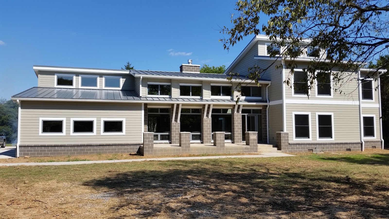 Front exterior of a residential building in East Tennessee with grey siding, white trim, a metal roof, and a grey block foundation.