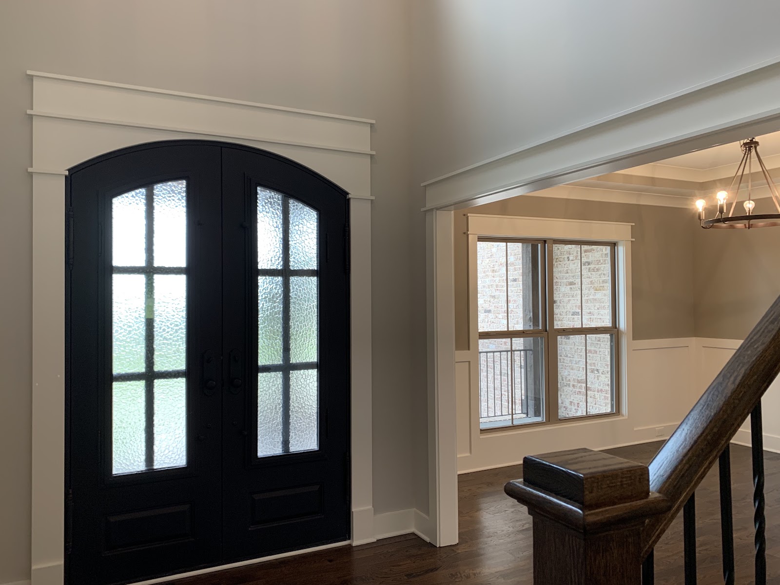 Entryway in The Chai House featuring black double doors with frosted glass panes and white trim, with a staircase railing in the foreground.