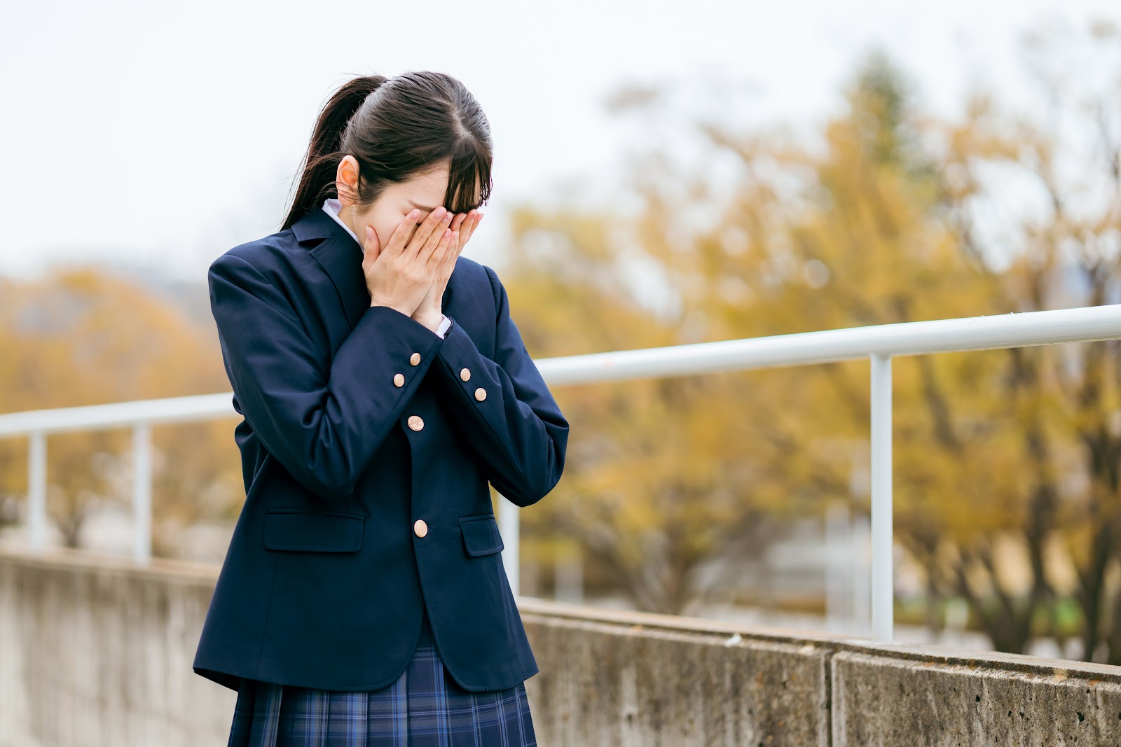 制服姿で顔を覆い俯く女子生徒のイメージ