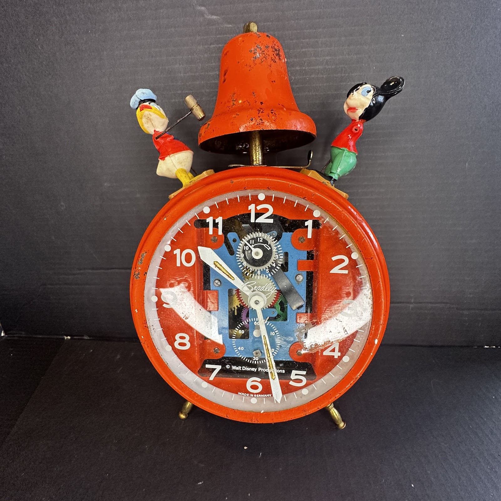 Bradley animated alarm clock with red painted tin casing, skeleton dial showing internal gears, and plastic Mickey Mouse and Donald Duck figures on top, Donald posed mid-swing with a hammer toward the bell