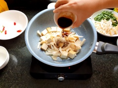 Cho thêm đậu hủ vào chiên sơ cho săn lại trước. Sau đó cho thêm nấm đã xé sợi vào cùng rồi đảo đều. Cho gia vị 1/2 muỗng canh hạt nêm chay, 2 muỗng canh nước tương, 1 muỗng canh đường, 1 muỗng cà phê tiêu.