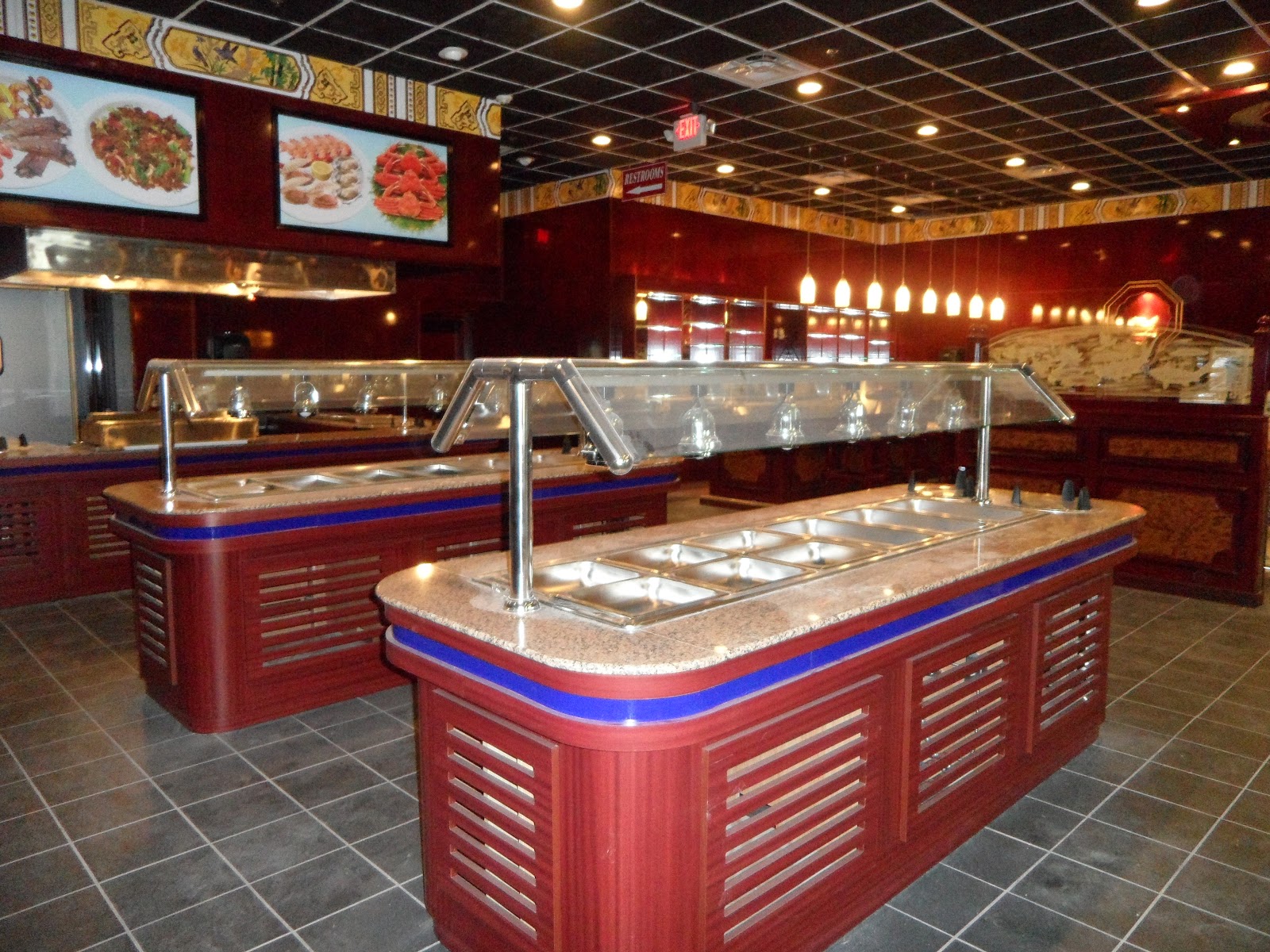 Two red wood-paneled buffet stations with stainless steel food pans and glass sneeze guards on a tiled floor.