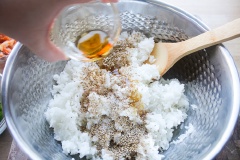 Hành lá mua về rửa sạch, loại bỏ phần đầu trắng, cắt hành lá thành các khúc chéo dài khoảng 1.5cm. Cho cơm nóng ra một cái tô lớn, thêm 1 muỗng cà phê muối, 2 muỗng canh mè trắng rang, 2 muỗng canh dầu mè, 1 muỗng canh giấm vào. Dùng muỗng gỗ trộn đều lên.